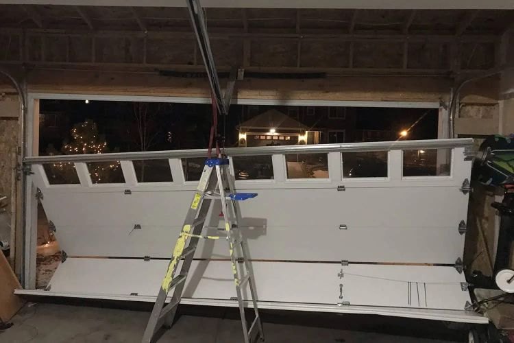 Sectional garage door lifted off its tracks and rested on a stepladder inside the garage during a night call, the open doorway and the street visible beyond
