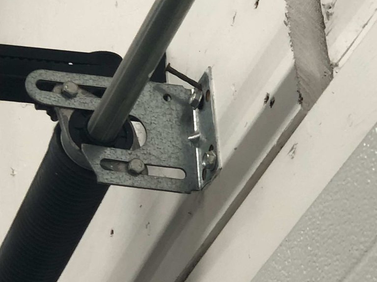 Centre bearing plate carrying the torsion shaft, bolted to the header above a garage door, with the spring end fitting beside it